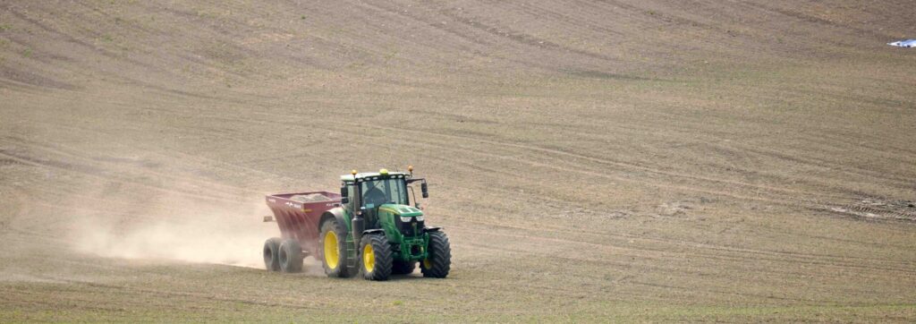 A tractor pulling a trailer in the middle of an empty field.